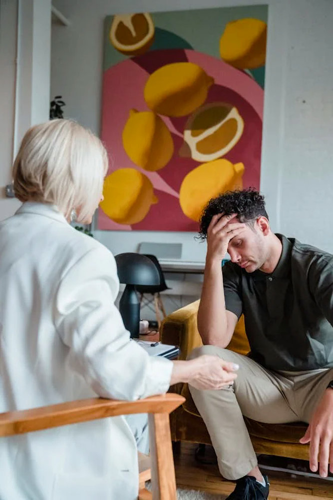 A young man holding his head in his hand during a counseling session with a therapist.