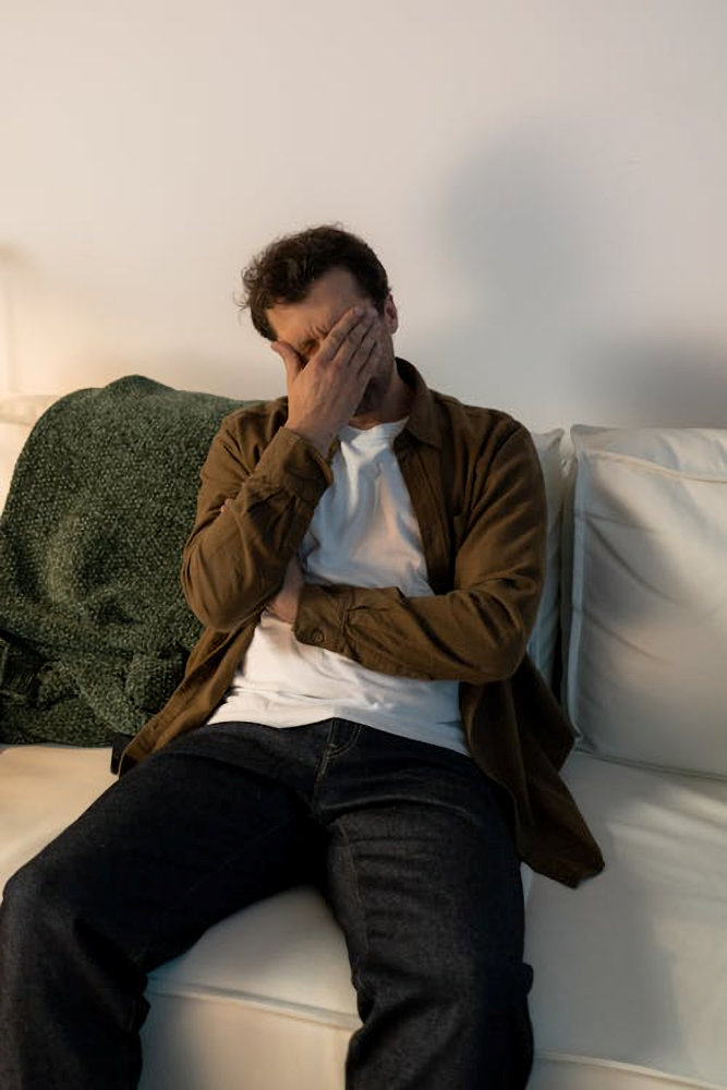 A man sitting on a couch with his head in his hand, appearing distressed.